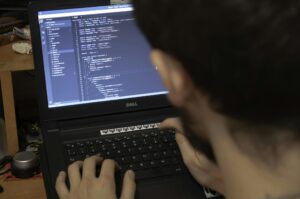 Close-up view of a programmer typing code on a laptop in a workspace.