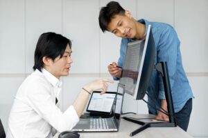 Two Asian men collaborating on a project using computers in an office.